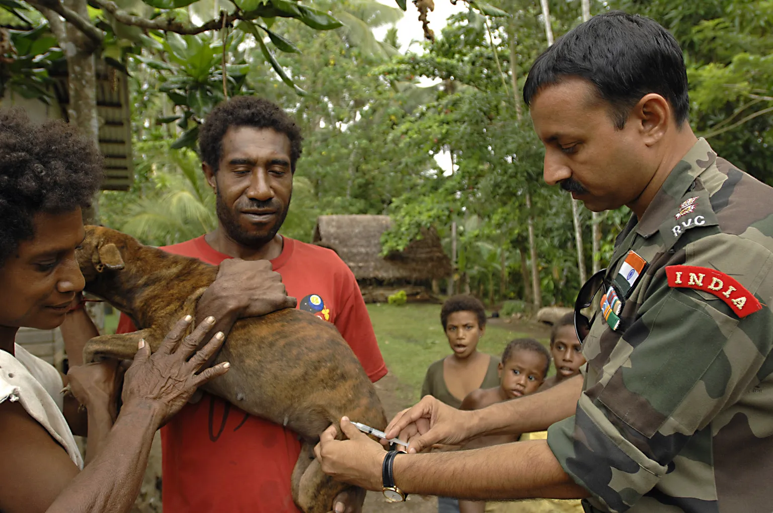 An Indian Army veterinarian gives a rabies vaccination to a family dog while people hold the animal.