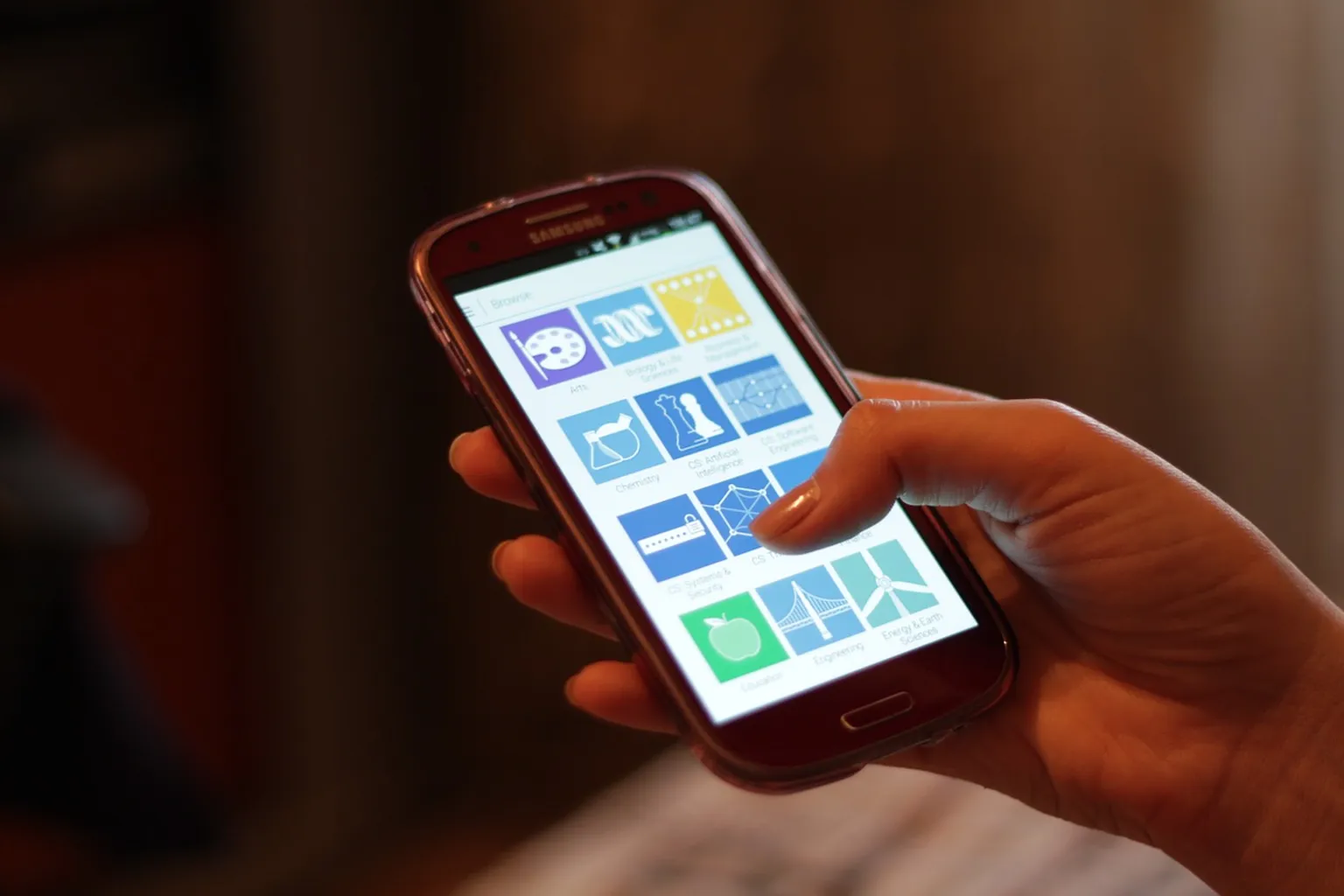 A hand holds a smartphone displaying a grid of app icons.