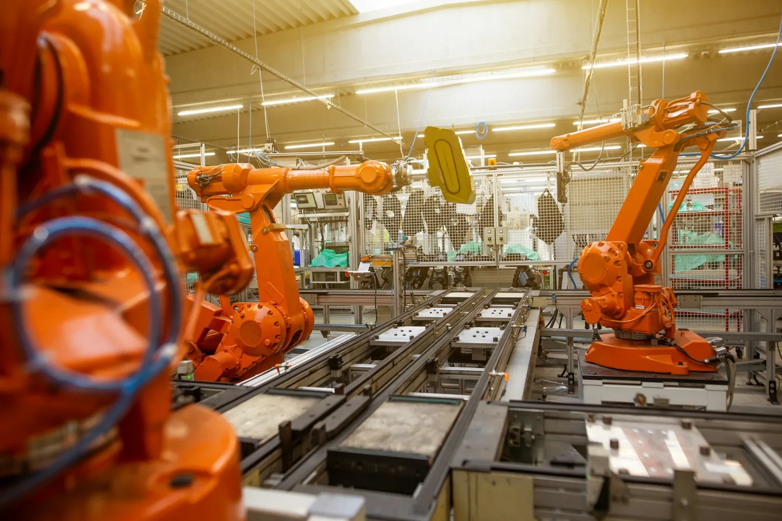 Orange industrial robot arms working along a factory assembly line.