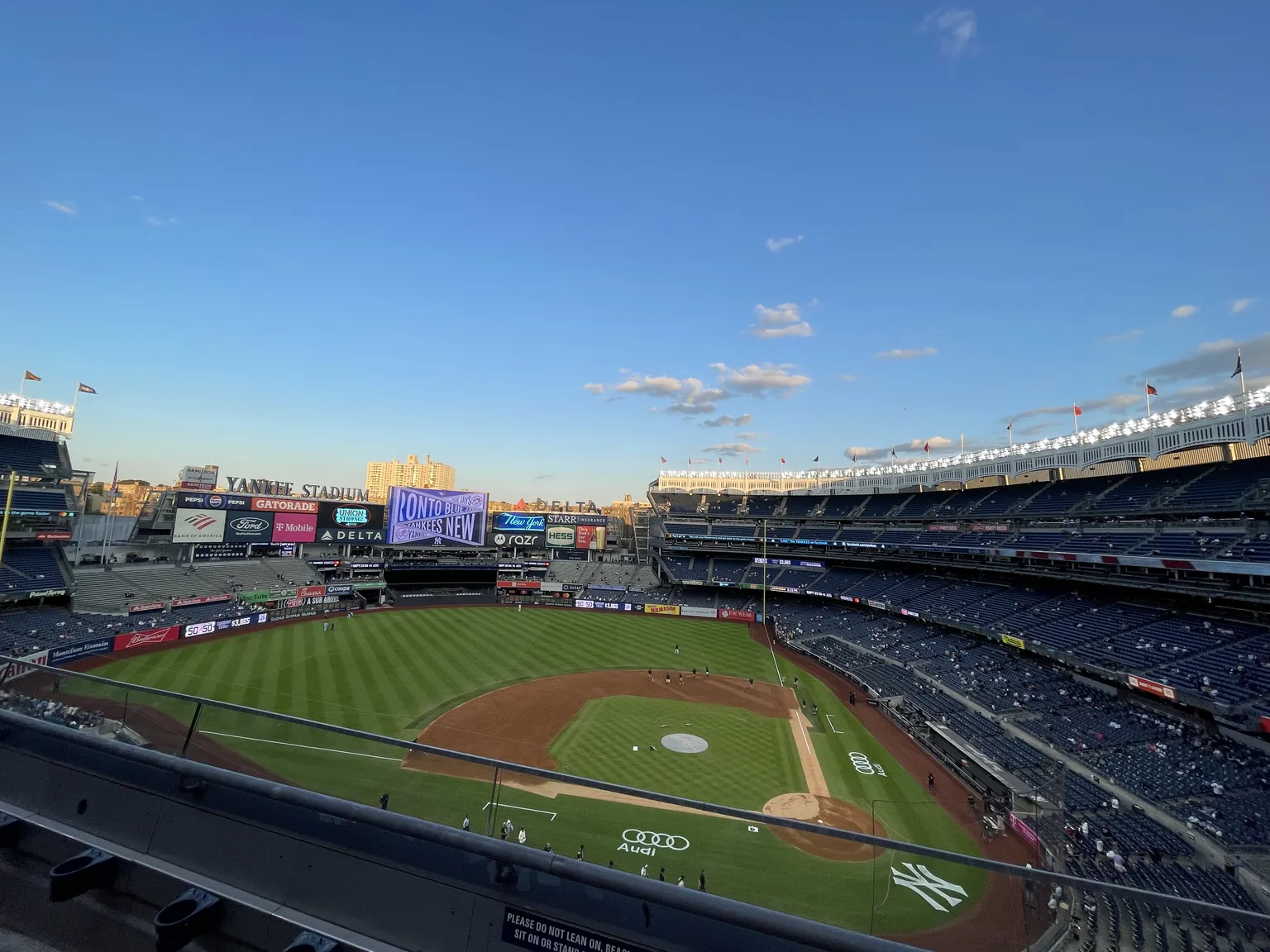A wide view from the upper deck of Yankee Stadium, with the baseball field and stands below a blue sky.