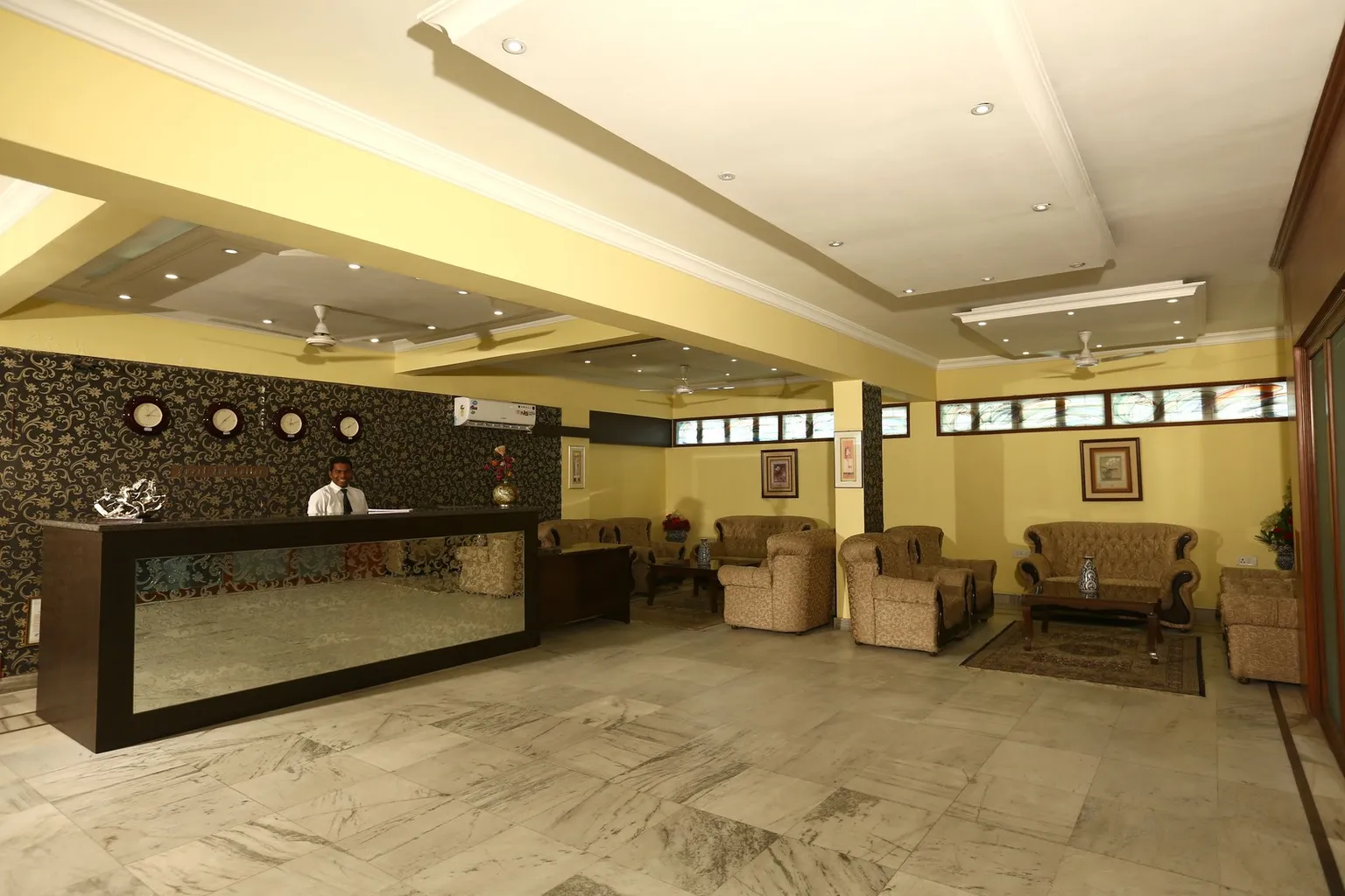 A hotel employee stands behind the front desk in a hotel lobby.