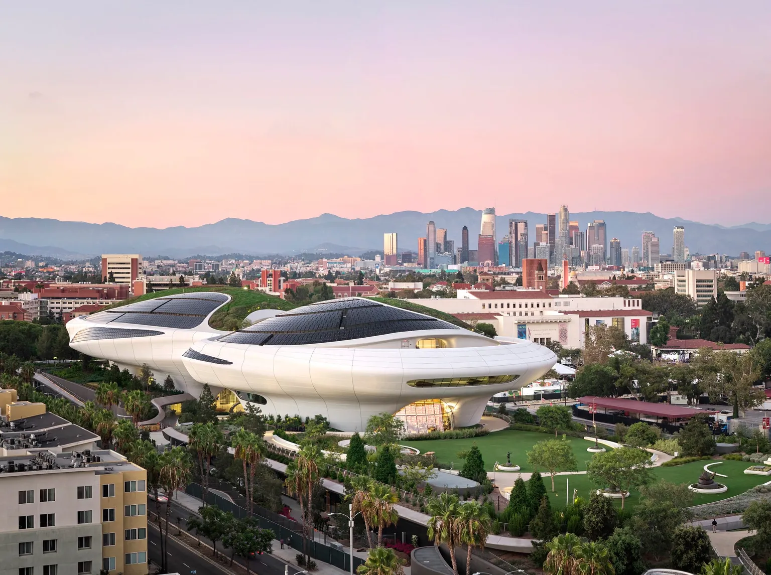Aerial view of the Lucas Museum of Narrative Art in Exposition Park with Los Angeles skyline behind it.