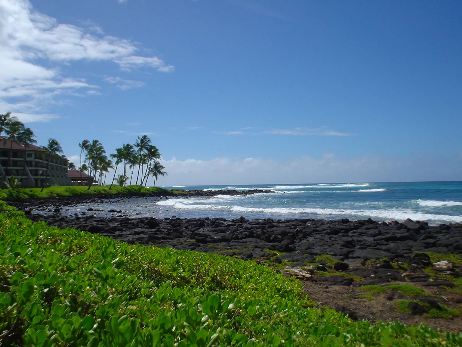 Archival 2004 photograph of Poipu Beach on Kauaʻi’s South Shore, showing a rocky coast, palms and a resort; not a post-storm image.