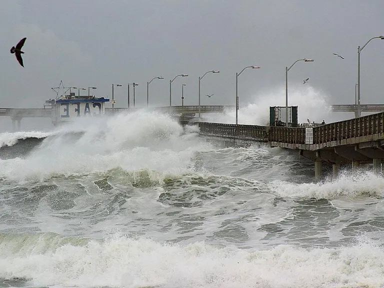 Storm waves crash against a pier, illustrating the coastal-weather risks associated with a strengthening El Niño
