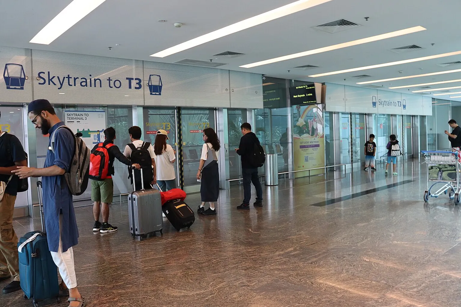 Passengers with luggage wait near the Skytrain to Terminal 3 at Singapore Changi Airport.