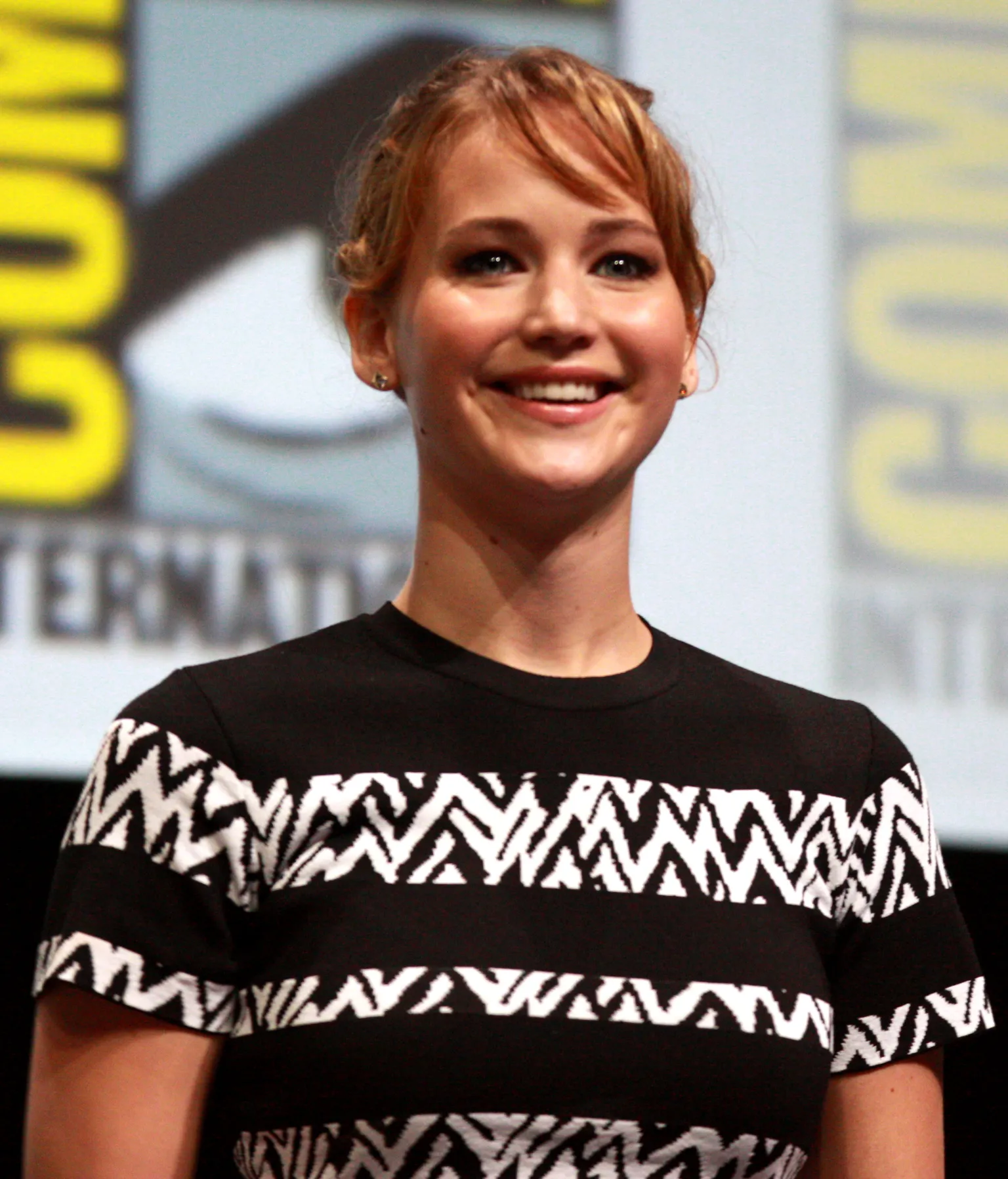 Jennifer Lawrence smiles while speaking at San Diego Comic-Con in 2013, wearing a black patterned shirt.