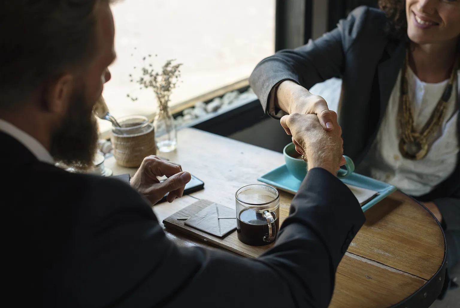 Two people seal a business meeting with a handshake across a cafe table.